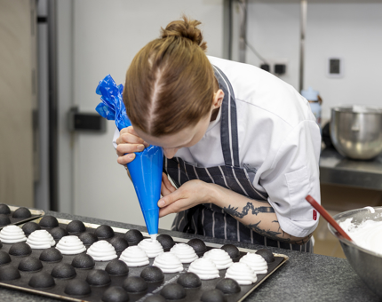 A Chef is piping meringue onto moulds ready to go in oven. 