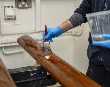 A close up of a hand holding a paint brush varnishing a handrail. 