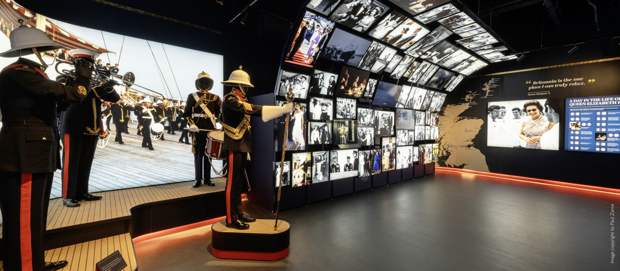 Inside the new Visitor Centre at Britannia. There is a floor to ceiling cascade wall of images and video and mannequins wearing uniforms of the Royal Marines' Band.