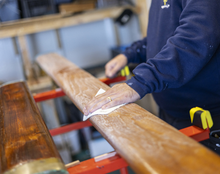 A close up of a hand sanding a wooden handrail. 