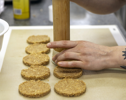 A close up of a chefs hands holding a rolling pin, making bases for cheesecakes. 