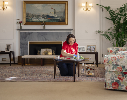 A Housekeeper is polishing a glass-topped table in the Drawing Room aboard Britannia.