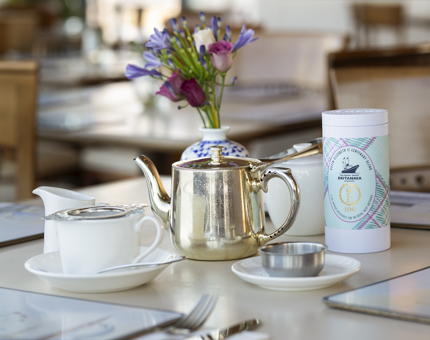 A table in the Royal Deck Tearoom is set with a silver teapot, cup and saucer, cannister of tea and small vase of flowers. 