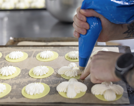 A close-up of a chef piping cream onto pastry rounds in Britannia's Galley. 