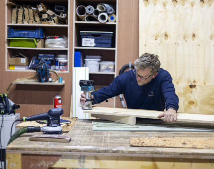 A maintenance team member is in the workshop cutting wood to make shelving. 