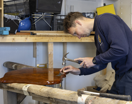 A man is using a hammer to reattach engraving to a wooden plaque in the workshop. 
