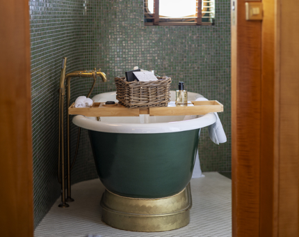A roll-top bath in a bathroom at Fingal. A basket containing toiletries sits atop a wooden bath tray. 