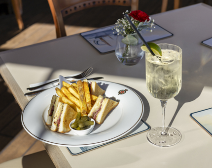On a table in the Royal Deck Tearoom there is a plate with a sandwich, fries and pickles, along with a spritz drink. 
