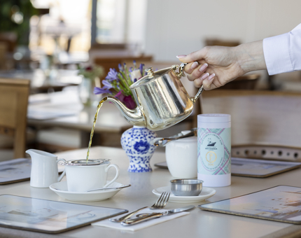 A had is holding a silver teapot and is pouring  tea into a teacup on a table int the Royal Deck Tearoom in Leith. 