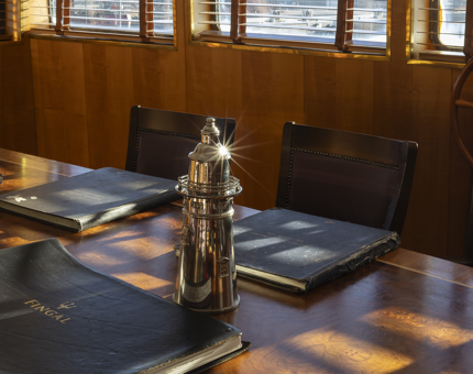 The Bridge aboard Fingal. The table has a silver lighthouse ornament and log books on it. The sun is shining through the window. 