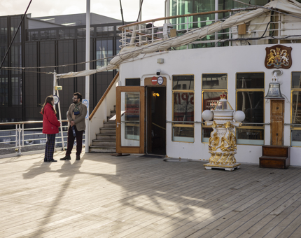 Two people are standing and talking on Britannia's Verandah Deck in the Port of Leith. 