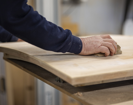A close up of a hand sanding a wooden hatch from a fast motor launch boat. 