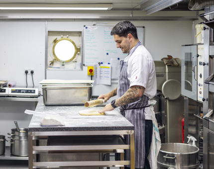 A chef is in the Galley aboard Britannia rolling out pastry. 