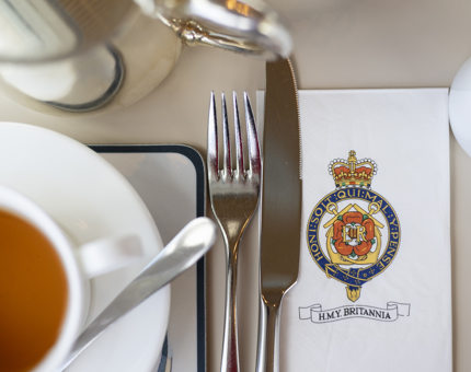 A Britannia Crested Napkin sits under a knife and fork.