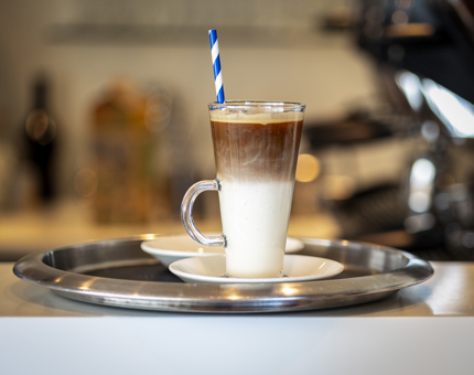 An iced coffee sitting on a silver tray with a blue and white straw. 