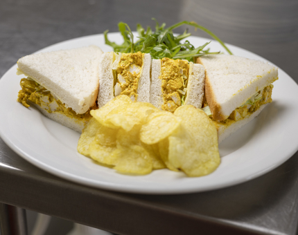 A plate with a Coronation chicken sandwich and crisps on it. 