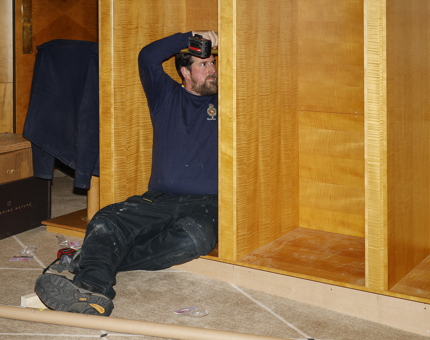 A maintenance man sitting on the floor holding a drill creating a new luggage store. 