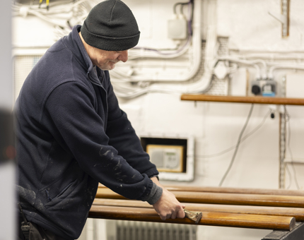 Maintenance team member scraping varnish off of handrails. 