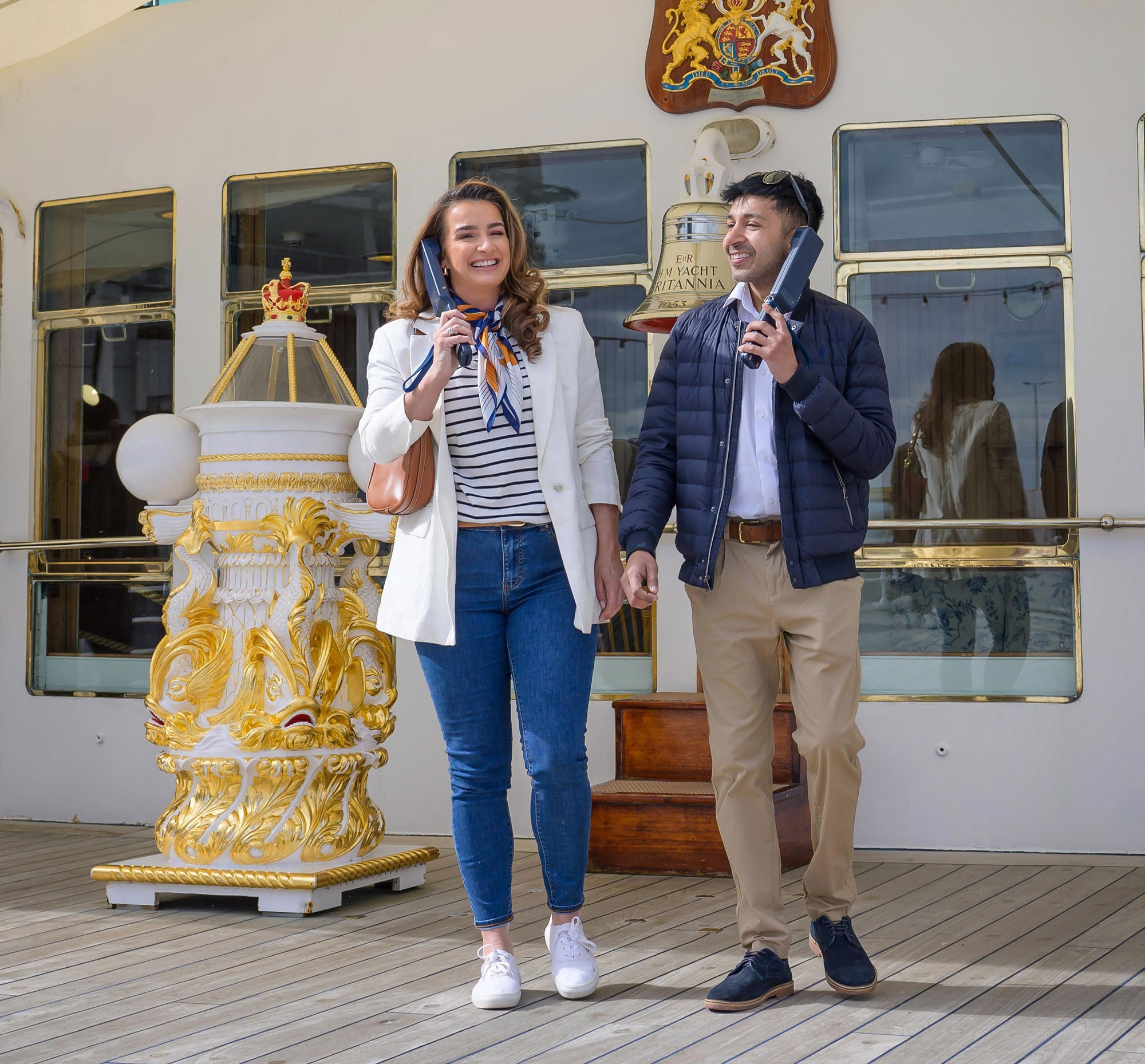 A man and woman are listening to audio guide handsets on Britannia's Verandah Deck in the Port of Leith.