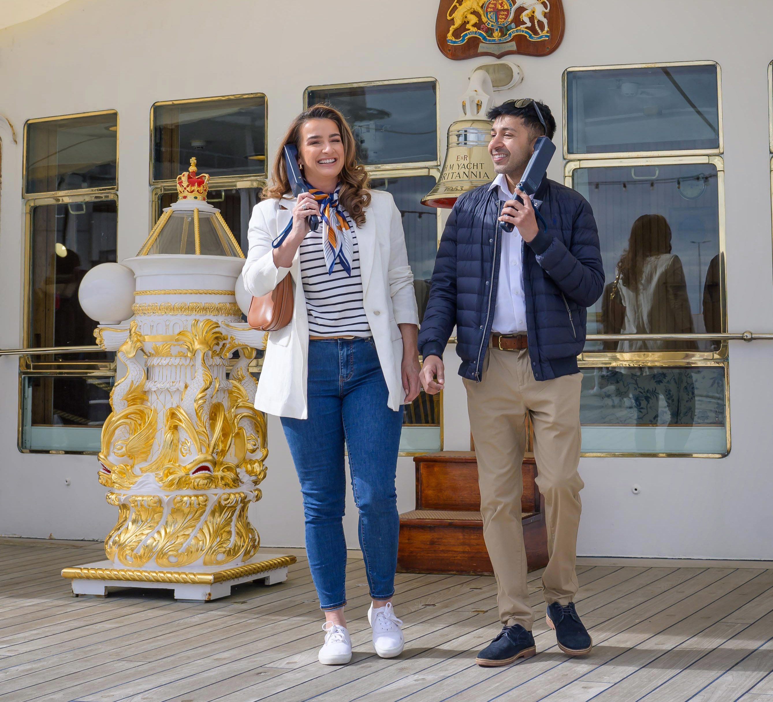 A man and woman on the Verandah Deck of The Royal Yacht Britannia listening to audio guide handsets.