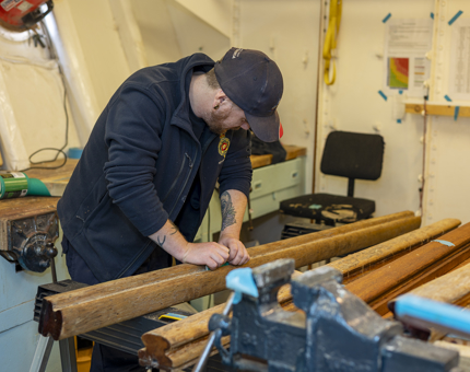 A Maintenance team member is holding sandpaper, sanding varnish off of wooden handrails.