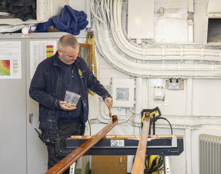 A Maintenance man is in the workshop varnishing wooden handrails. 