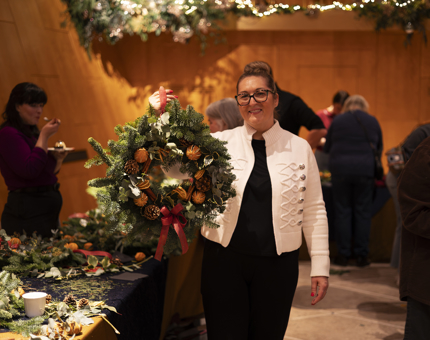 A woman is holding up a finished Christmas wreath that she has made. 
