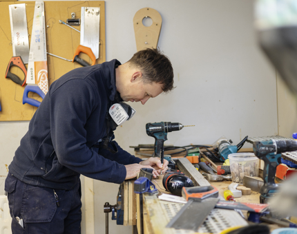 In the workshop, a Maintenance man is prepping To Drill Holes in a scupper board. 